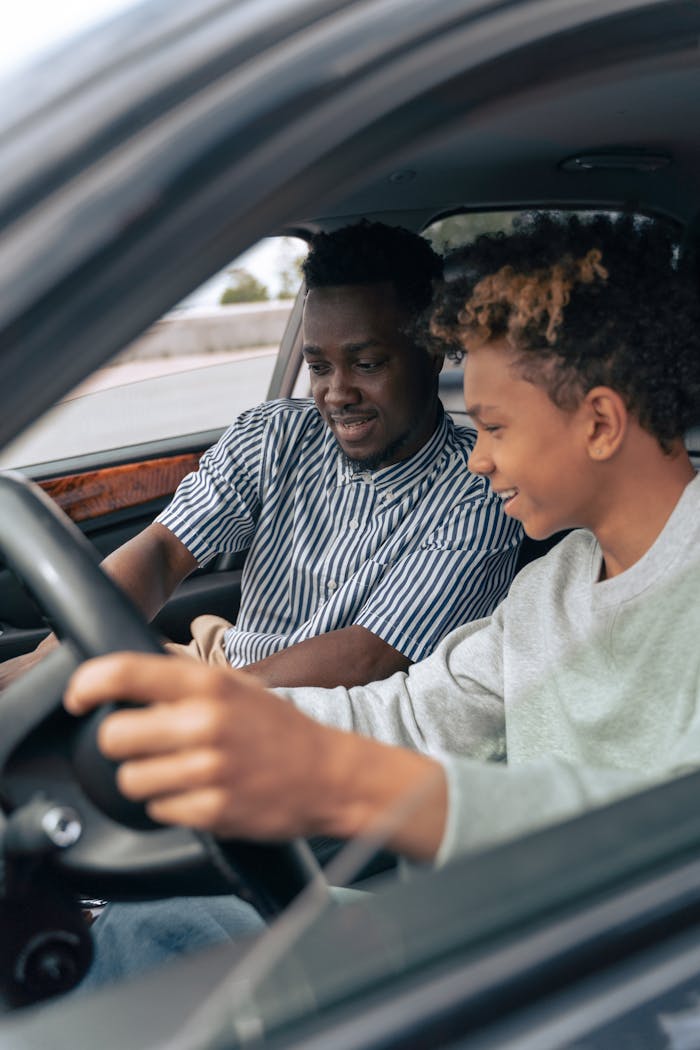 Father and teenage son sitting in a car, bonding while learning to drive.